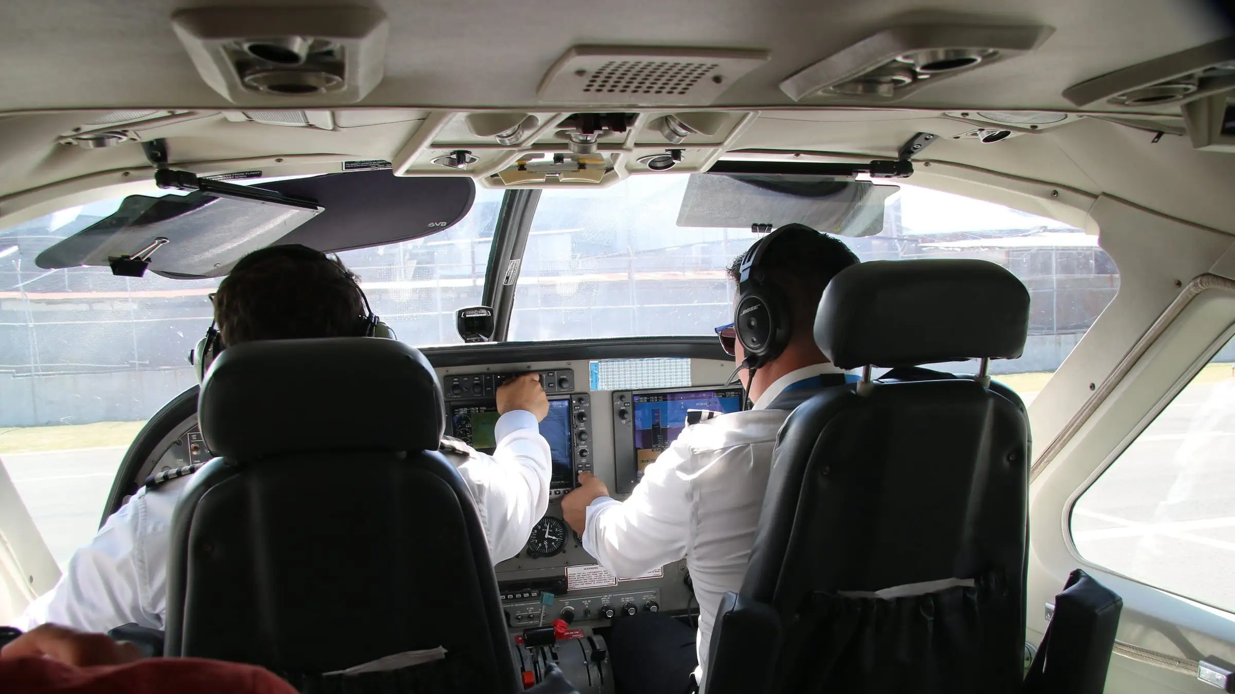 Two crew at the controls of a single-engine turboprop in cruise, seen from the cabin