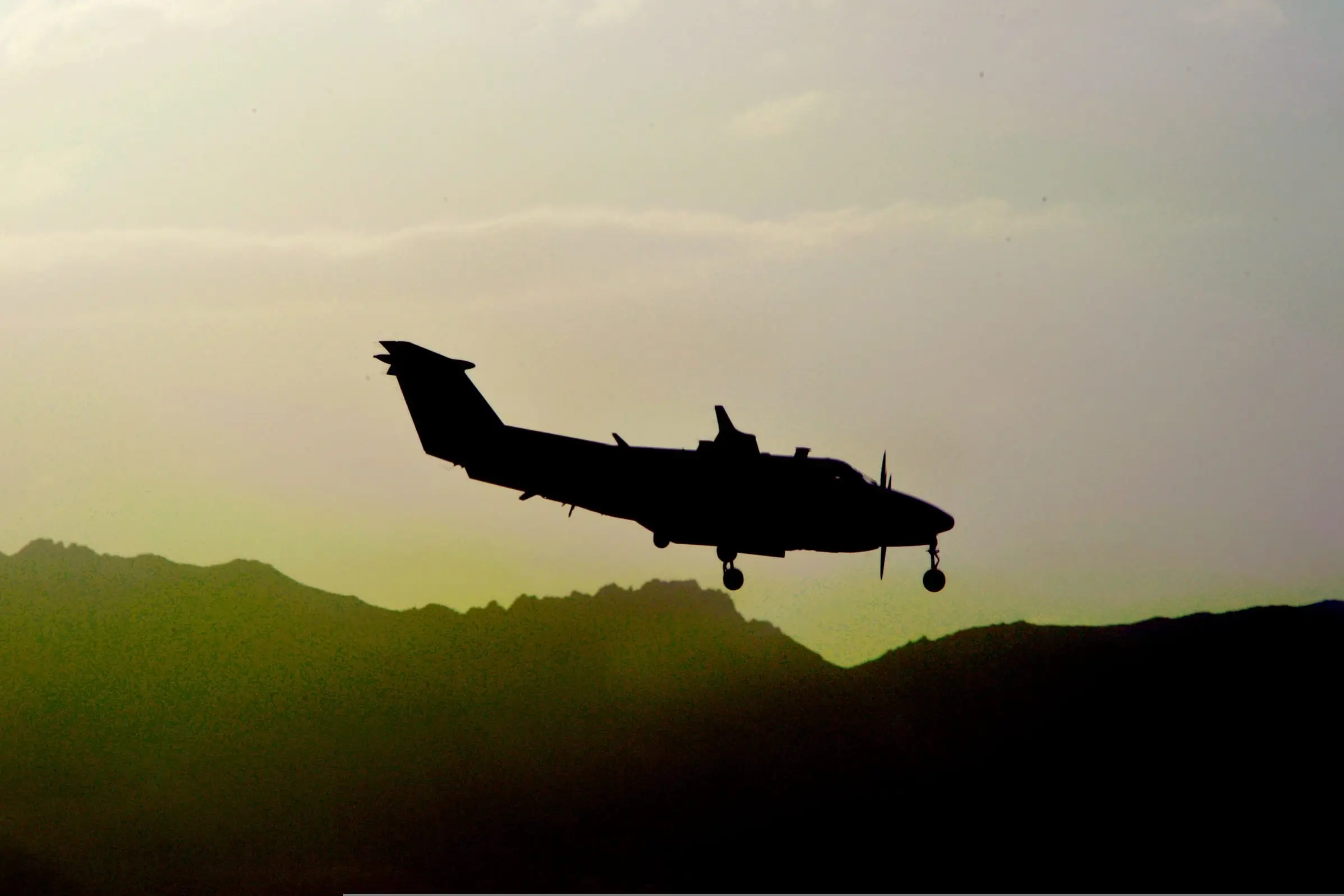 A King Air on final approach silhouetted against a mountain ridge at dusk