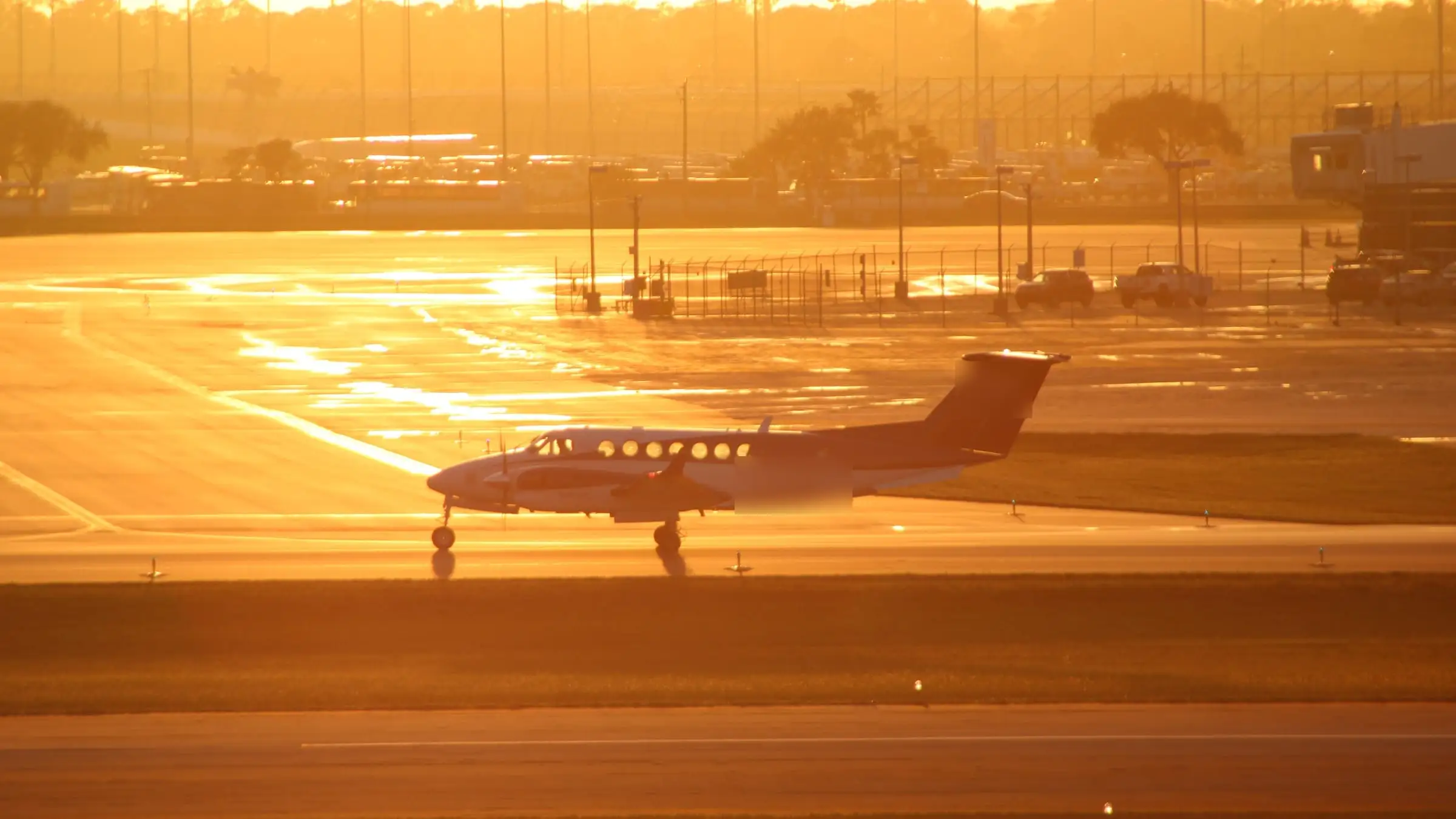 A twin-turboprop holding on a wet taxiway at dawn, backlit