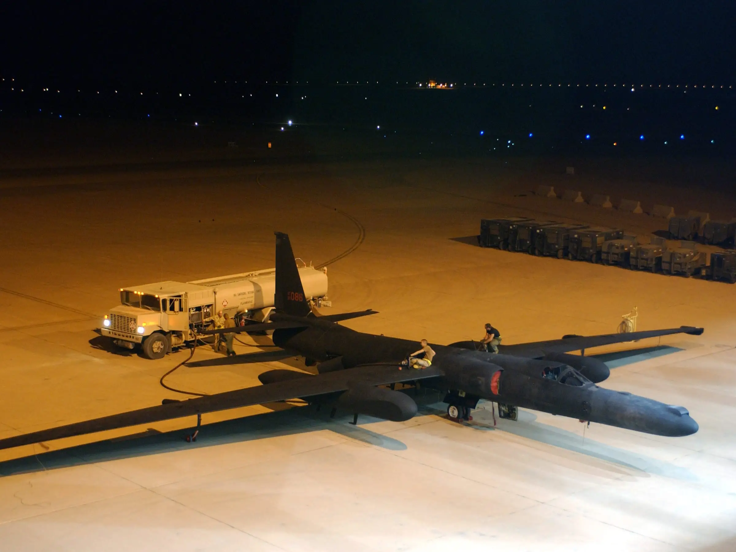 A refueler truck standing beside a parked aircraft at night with its hose run out across the apron