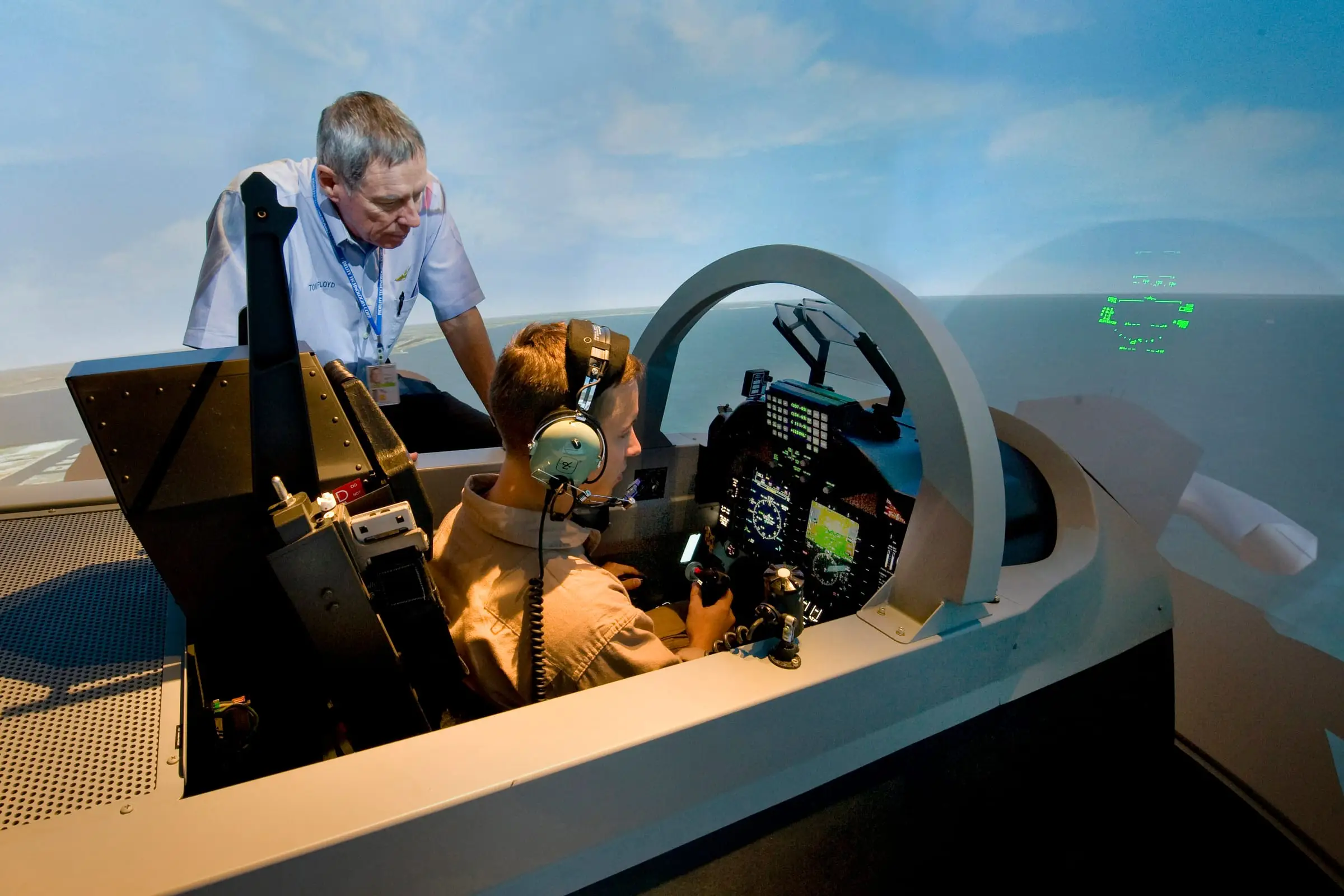 An instructor leaning into a flight simulator cockpit alongside a student pilot at the controls
