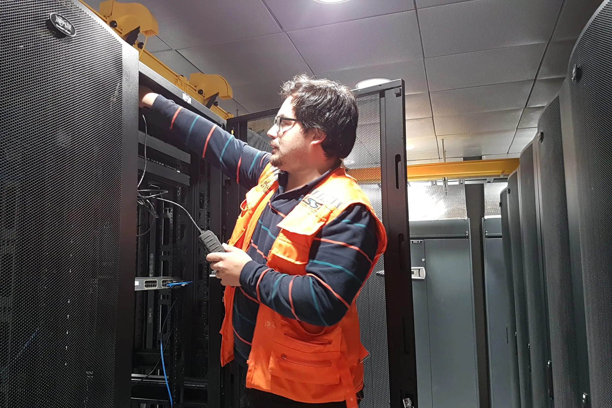 A technician routing cable into a server rack in a computer room lined with equipment cabinets