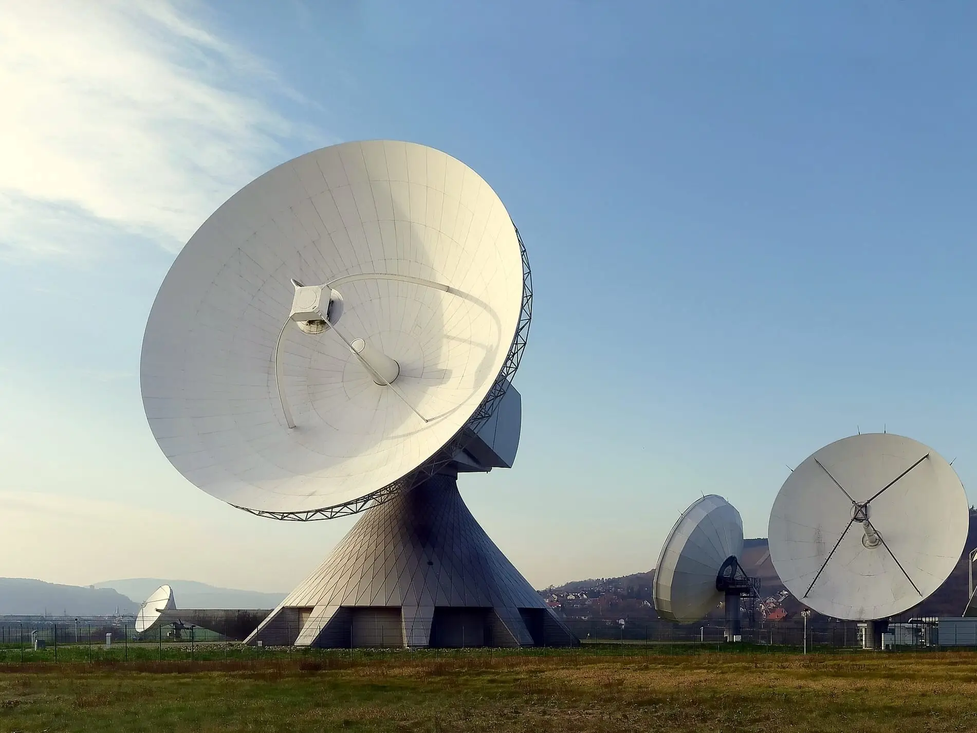 A line of large parabolic satellite antennas on their mounts at a ground station under open sky