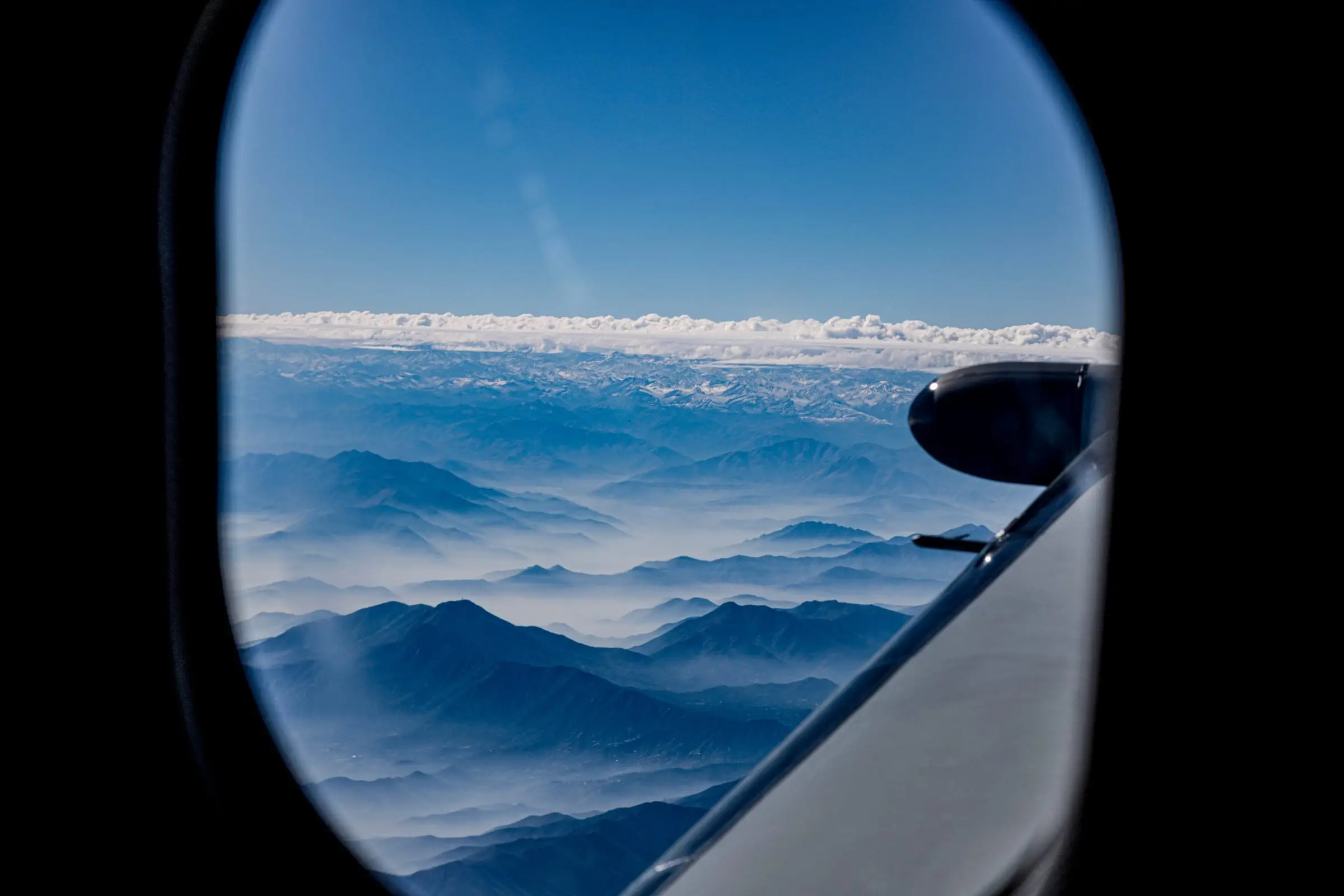 A hazed mountain range seen through a PC-12 cabin window with the wing in frame