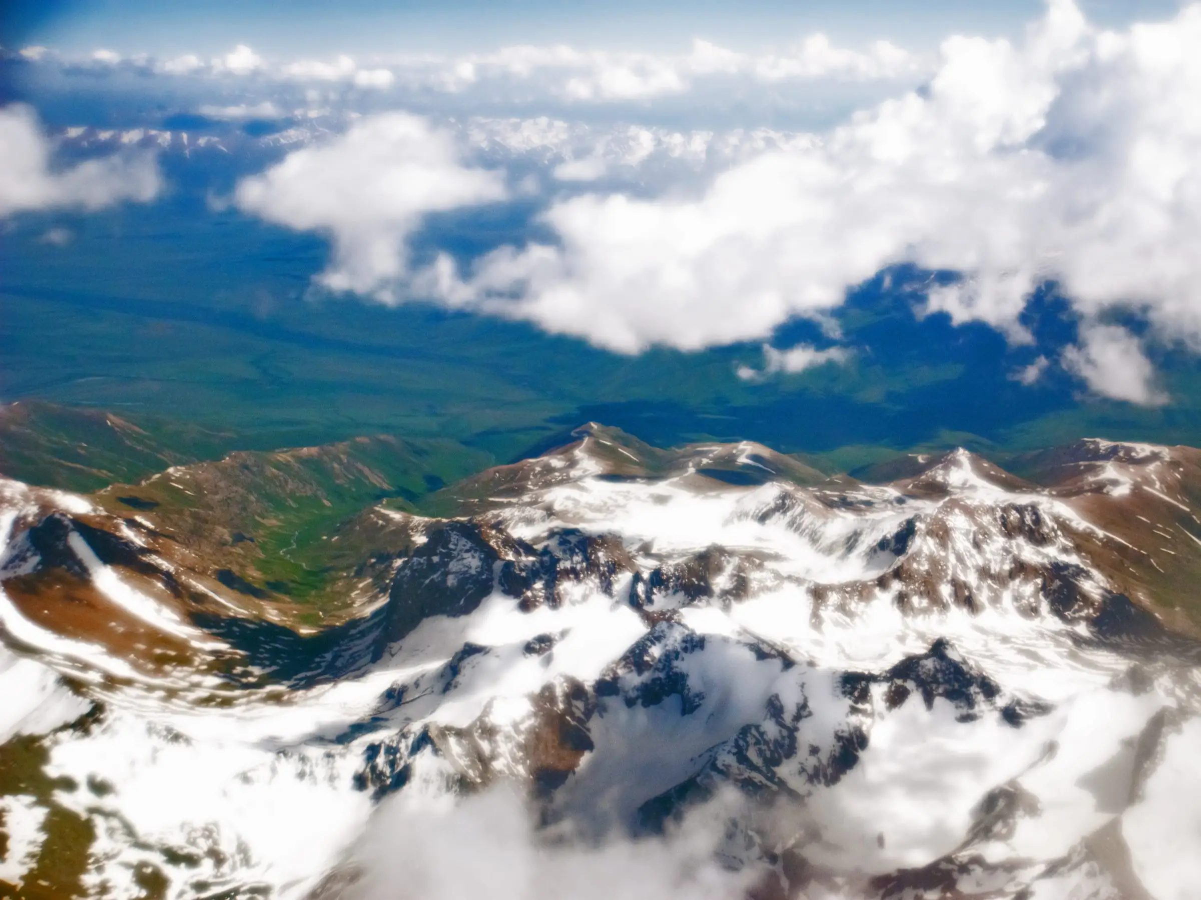 Snow-covered peaks breaking through cloud seen from high altitude