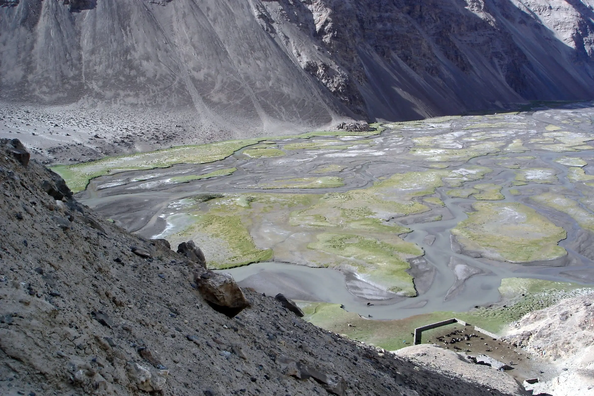 A braided river spread across a wide gravel valley floor below steep slopes
