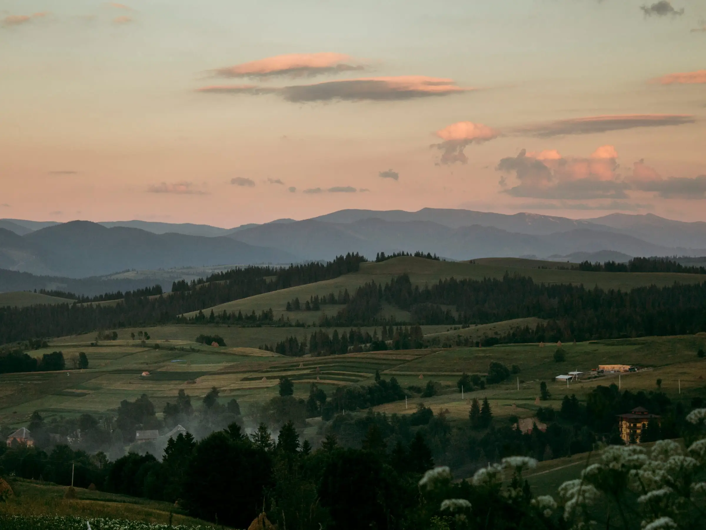 Rolling forested hills and cultivated ground fading into haze at dusk