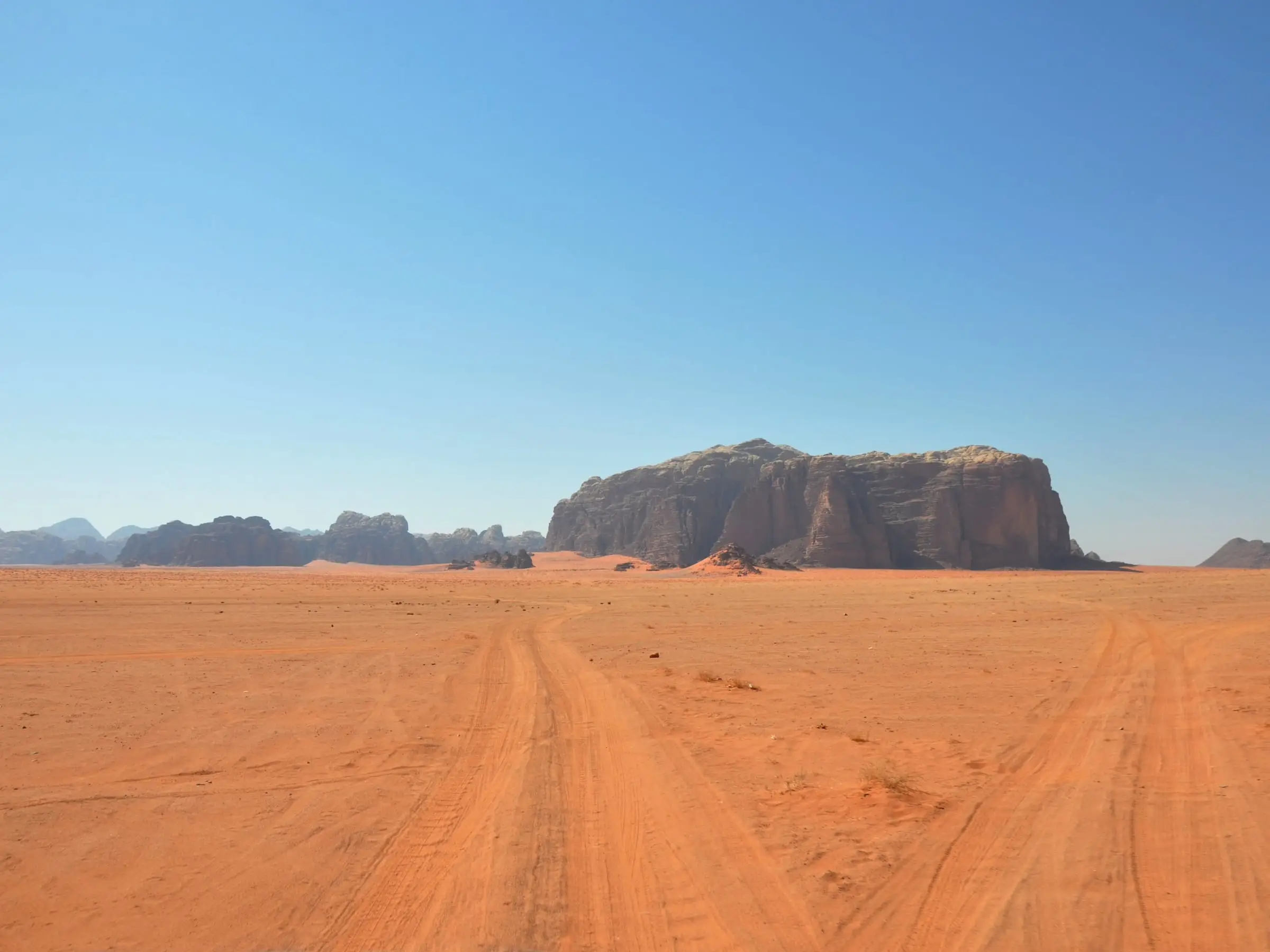 Vehicle tracks crossing open red desert toward an isolated sandstone massif