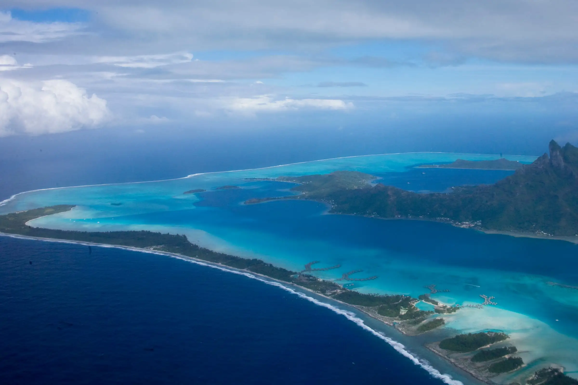 A volcanic island ringed by a barrier reef and lagoon, seen from the air