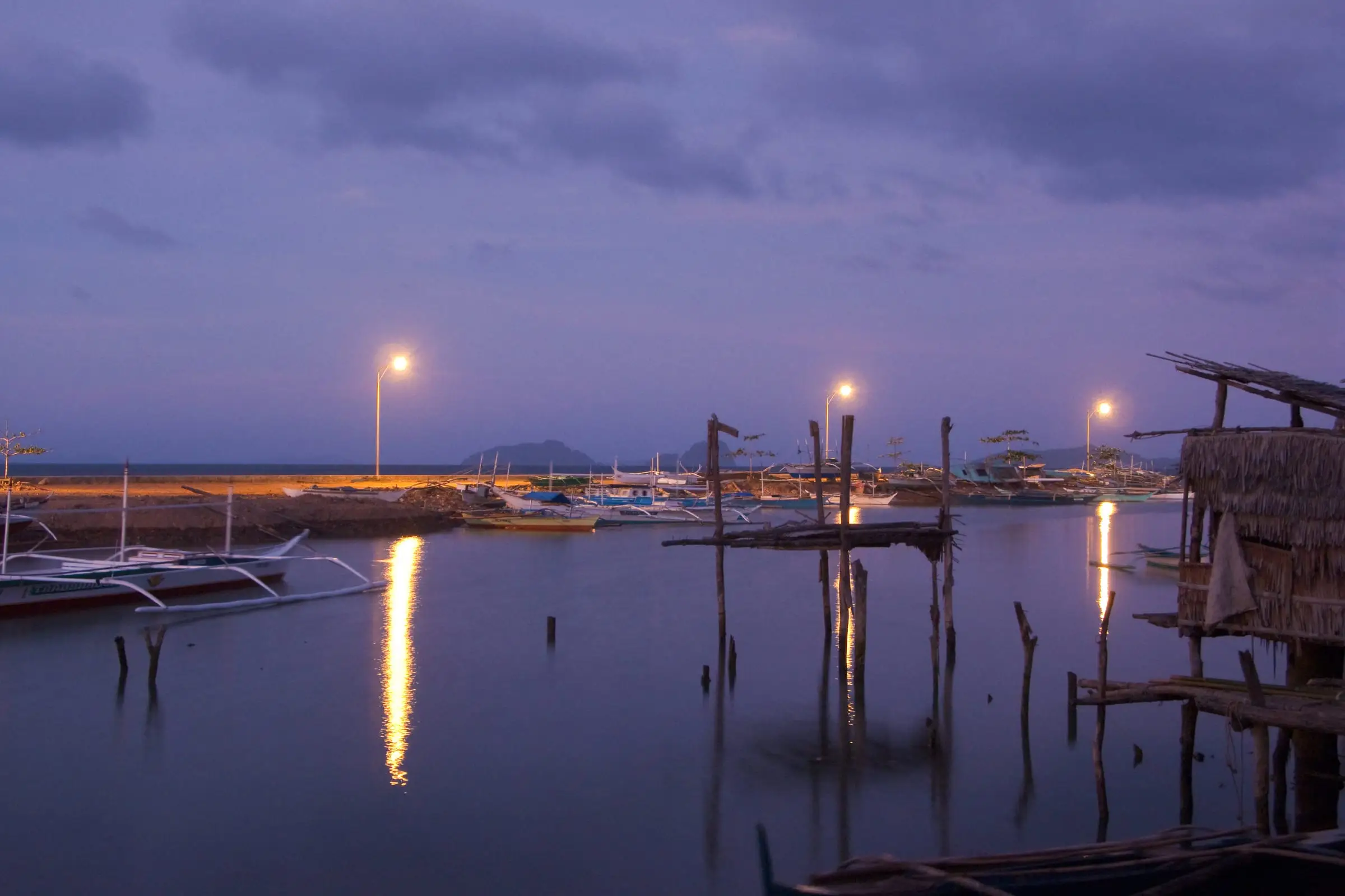 Small outrigger boats moored along a shallow waterfront at night
