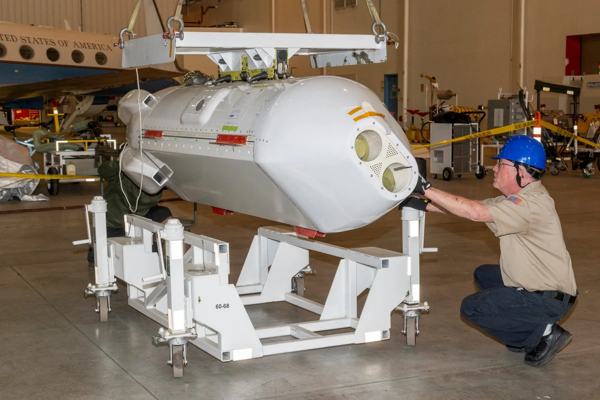 A sensor pod being lowered onto its wheeled handling cradle in a hangar