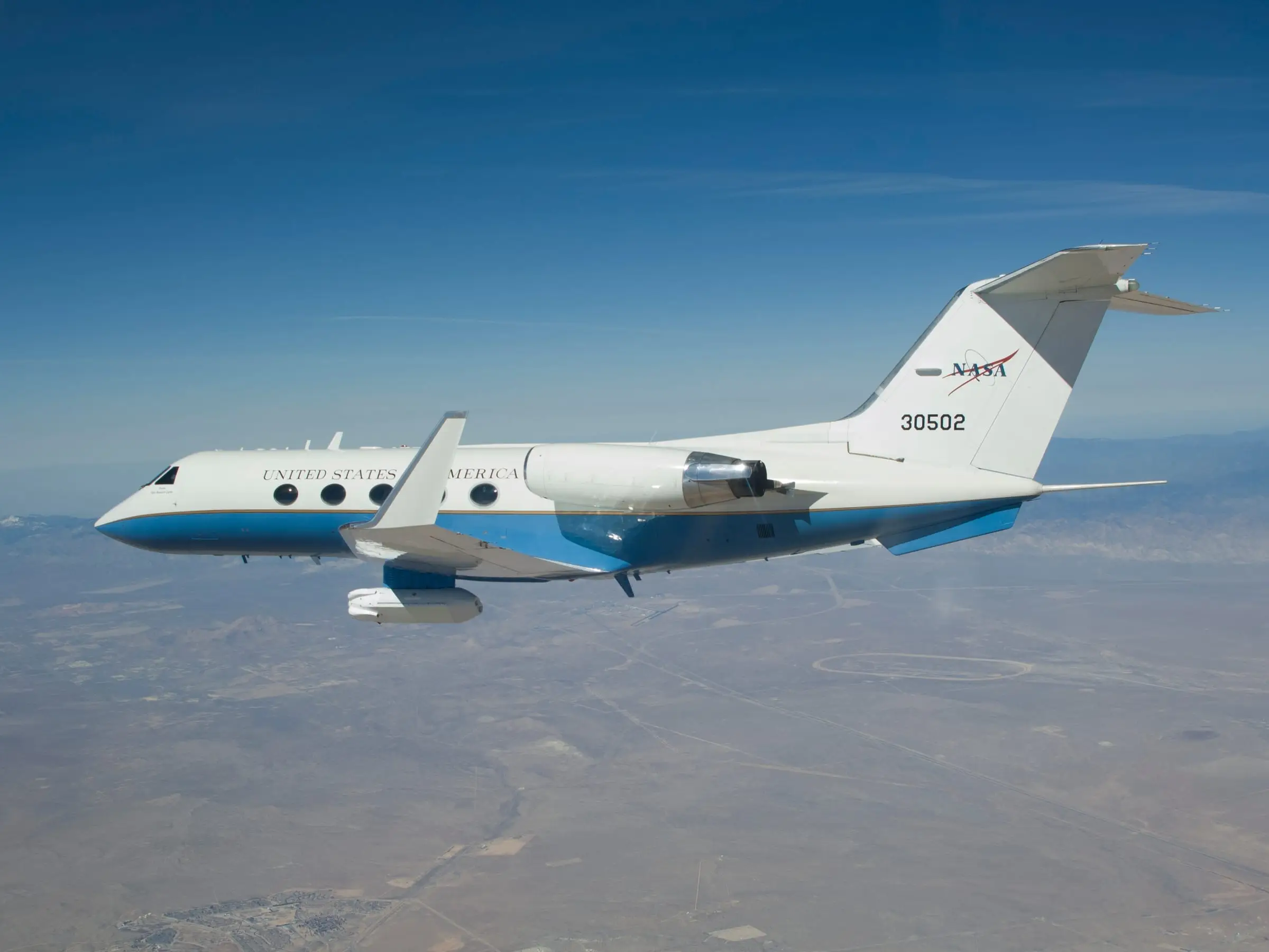 A twin-jet in flight carrying a large instrument pod under the center fuselage